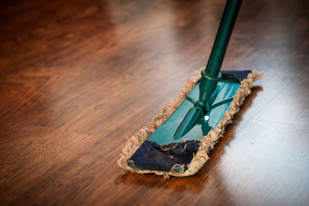 A mop with a green handle rests on a wooden floor, showcasing the effectiveness of a flooring service.