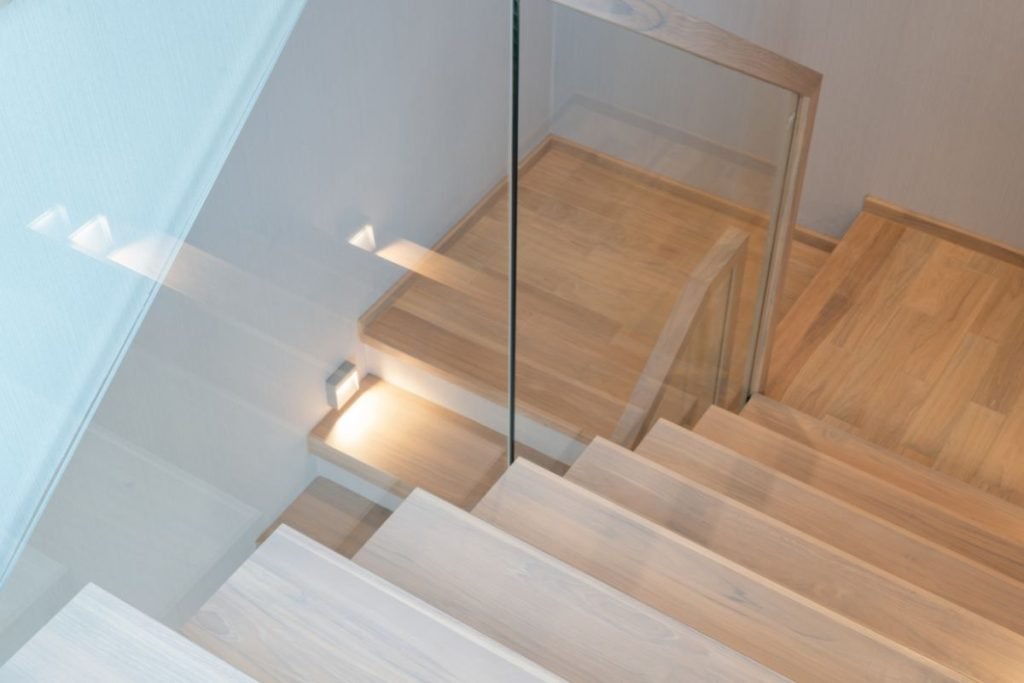 A modern staircase featuring wooden steps and a sleek glass railing, showcasing a blend of elegance and functionality.